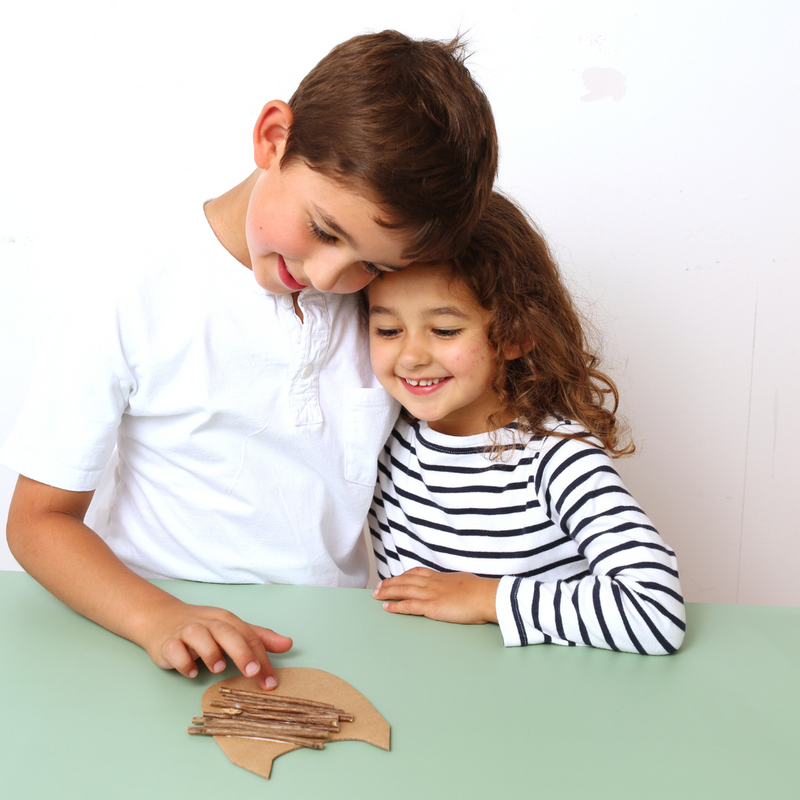 Two children sitting at a table with a cardboard craft project from a craft kit kids subscription box