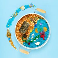 Sensory tray from My Mini Maker with rice and orange sand, toys, and a blue background. Perfect for imaginative play.