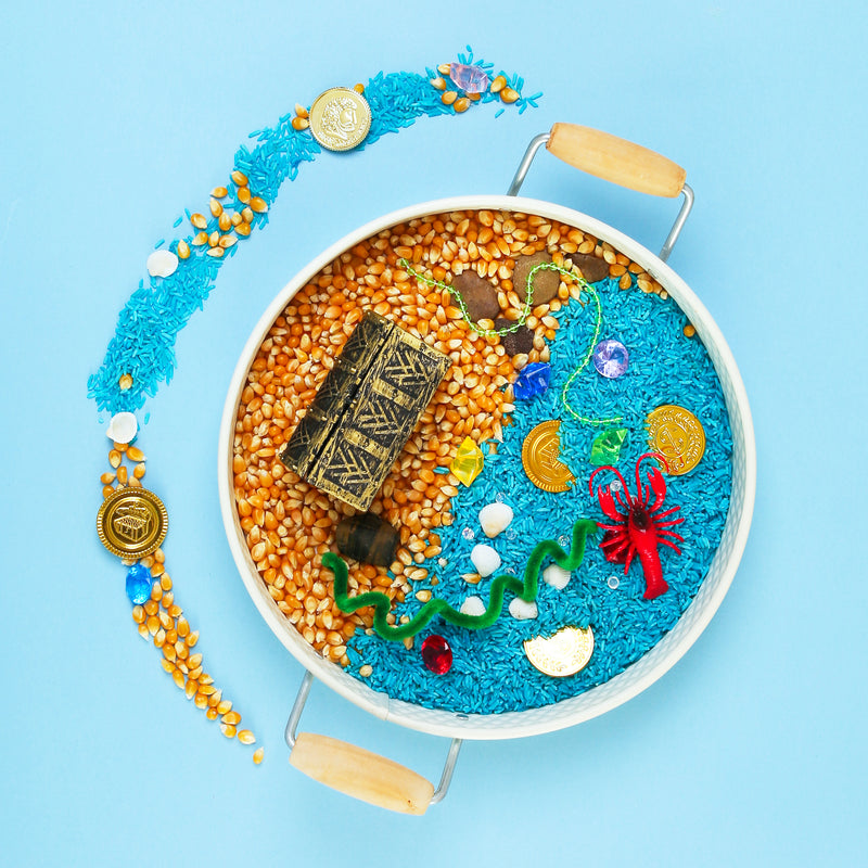 Sensory tray from My Mini Maker with rice and orange sand, toys, and a blue background. Perfect for imaginative play.