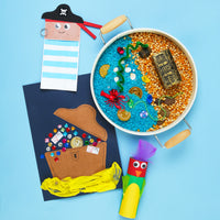 Children's sensory play setup with a pirate-themed sand tray, treasure chest, and crafts on a blue background.