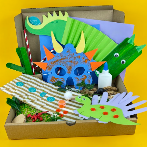 Dinosaur Activity Kit box with a blue dinosaur mask, green paper dinosaur, handprint dinosaur craft, sensory tray materials and glue