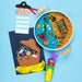 Children's sensory play setup with a pirate-themed sand tray, treasure chest, and crafts on a blue background.