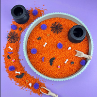 Halloween sensory tray filled with orange rice, purple pom-poms, small bones, bats, spider webs, ghosts and two black cauldrons, with a wooden scoop