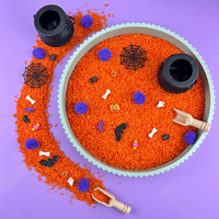 Halloween sensory tray filled with orange rice, purple pom-poms, bones, bats, spider webs and tiny ghosts, with two black cauldrons and a wooden scoop