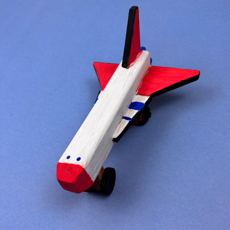 Wooden toy space shuttle with red and white design on a blue background. Perfect for kids to develop their independent problem solving skills.