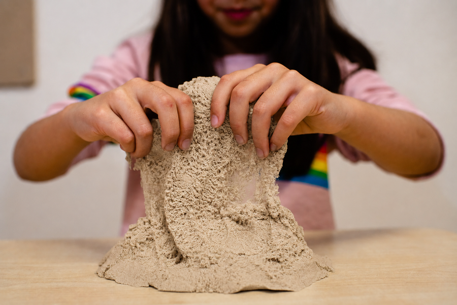 Child's hands moulding kinetic sensory sand on a table