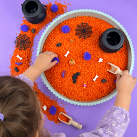 Child playing with the Halloween sensory kit, scooping orange rice and finding the spooky pieces hidden inside