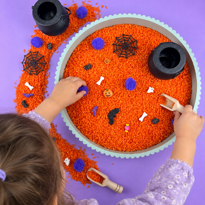 Child playing with the Halloween sensory kit, scooping orange rice and finding the spooky pieces hidden inside