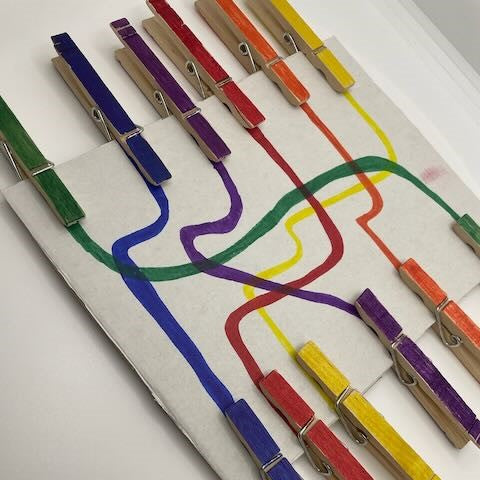 Colour matching activity: coloured pegs clipped to a cardboard square with wiggly matching lines