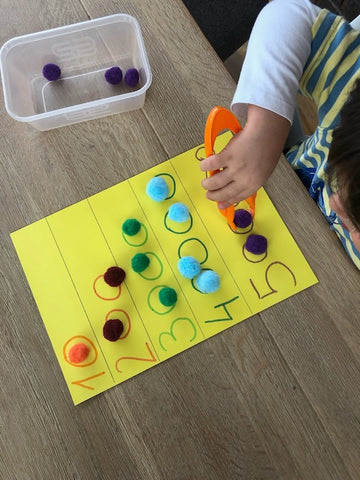 Child using tweezers to place pom-poms on a numbered sheet