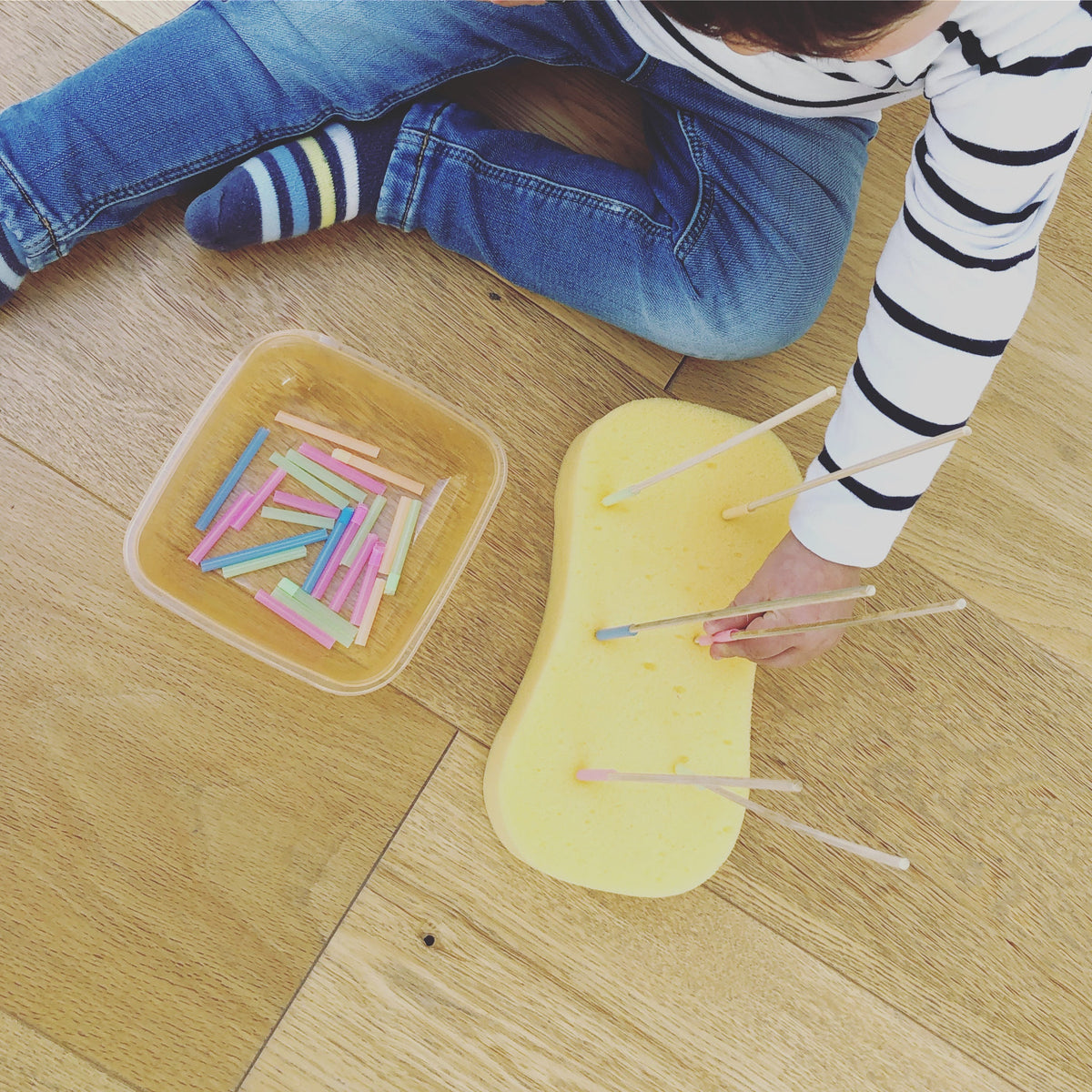 Toddler placing coloured straw pieces onto wooden sticks standing in a sponge