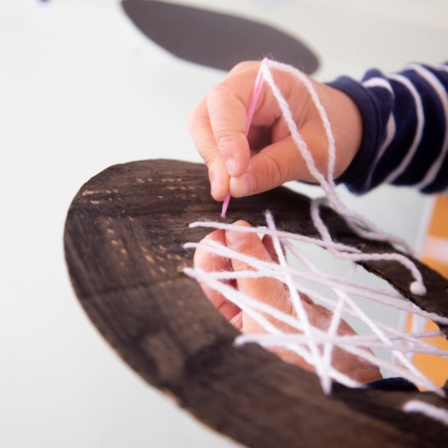 Child threading large wooden beads onto a pipe cleaner